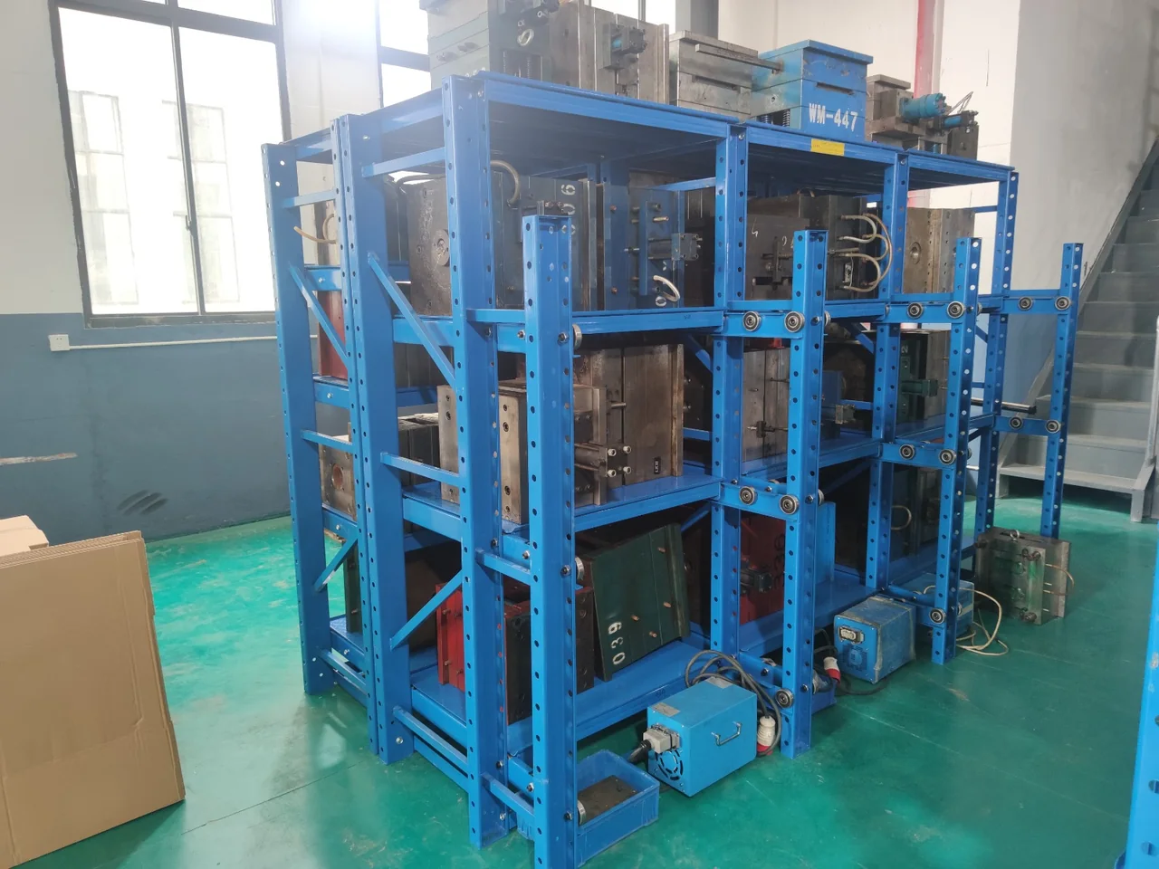 Rayonnage bleu à tiroirs accueillant des moules métalliques dans un atelier.